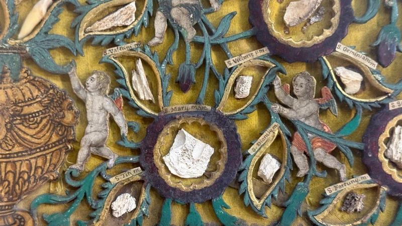 Quadro reliquiario con composizione in legno traforato in rilievo con putti e motivi vegetali.