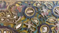 Quadro reliquiario con composizione in legno traforato in rilievo con putti e motivi vegetali.