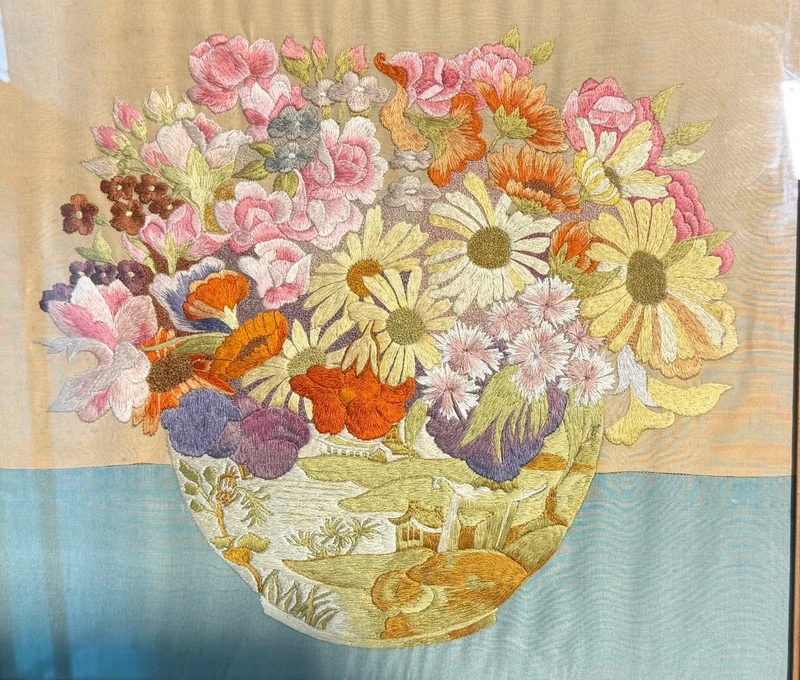 Framed panel featuring a vase of flowers embroidered on fabric.