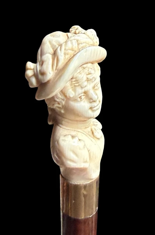 A walking stick with an ivory knob depicting a woman's bust wearing a hat.