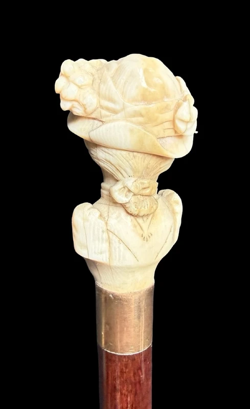A walking stick with an ivory knob depicting a woman's bust wearing a hat.