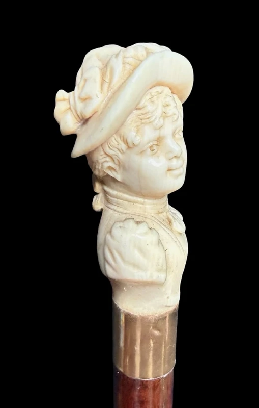 A walking stick with an ivory knob depicting a woman's bust wearing a hat.