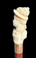 A walking stick with an ivory knob depicting a woman's bust wearing a hat.