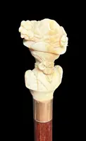 A walking stick with an ivory knob depicting a woman's bust wearing a hat.