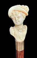 A walking stick with an ivory knob depicting a woman's bust wearing a hat.