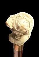 A walking stick with an ivory knob depicting a woman's bust wearing a hat.