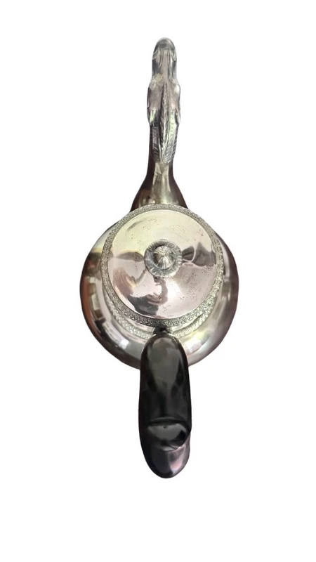 A silver coffee pot with a pear-shaped body on a circular base adorned with lanceolate leaves.