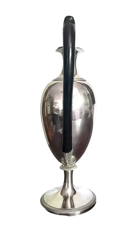 A silver coffee pot with a pear-shaped body on a circular base adorned with lanceolate leaves.