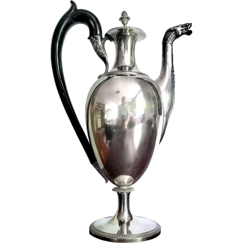 A silver coffee pot with a pear-shaped body on a circular base adorned with lanceolate leaves.