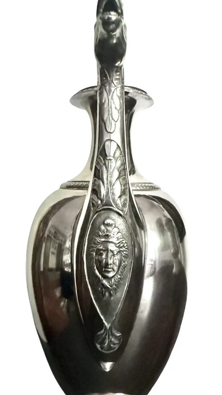 A silver coffee pot with a pear-shaped body on a circular base adorned with lanceolate leaves.