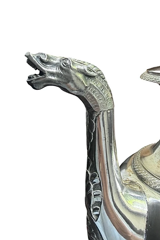 A silver coffee pot with a pear-shaped body on a circular base adorned with lanceolate leaves.