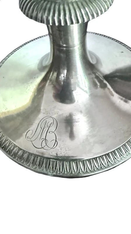 A silver coffee pot with a pear-shaped body on a circular base adorned with lanceolate leaves.