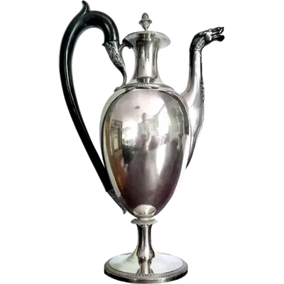A silver coffee pot with a pear-shaped body on a circular base adorned with lanceolate leaves.