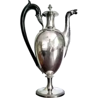 A silver coffee pot with a pear-shaped body on a circular base adorned with lanceolate leaves.