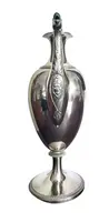 A silver coffee pot with a pear-shaped body on a circular base adorned with lanceolate leaves.