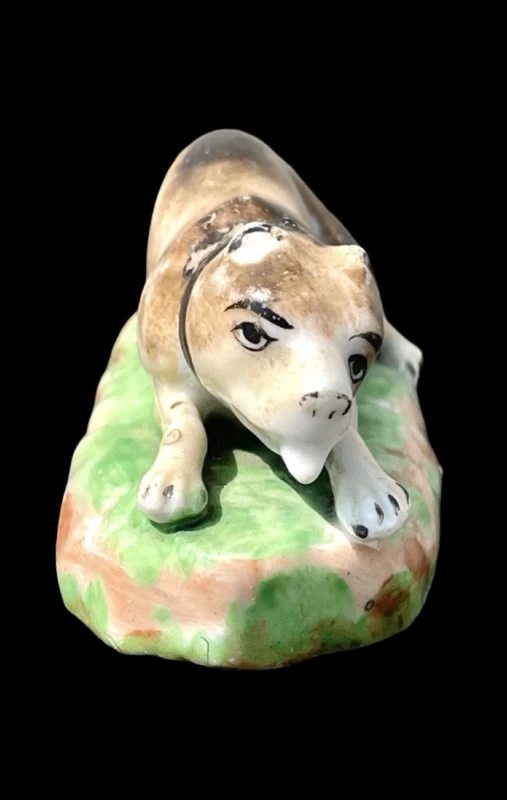Sculpture en porcelaine polychrome représentant un chien allongé sur un tapis d'herbe. Jacob Petit