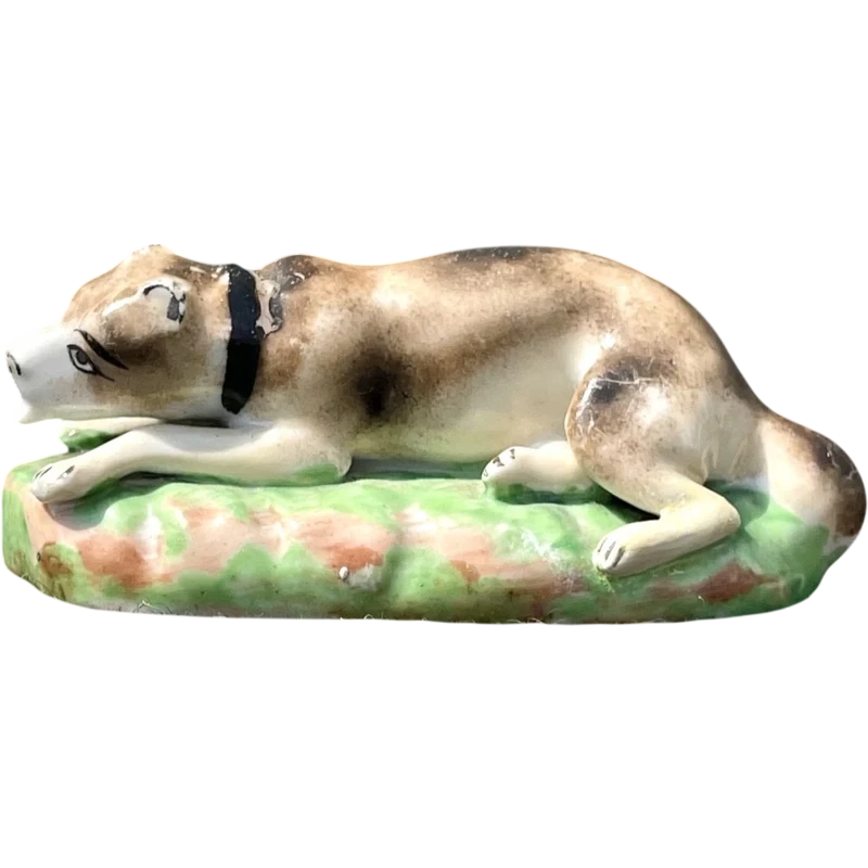 Sculpture en porcelaine polychrome représentant un chien allongé sur un tapis d'herbe. Jacob Petit
